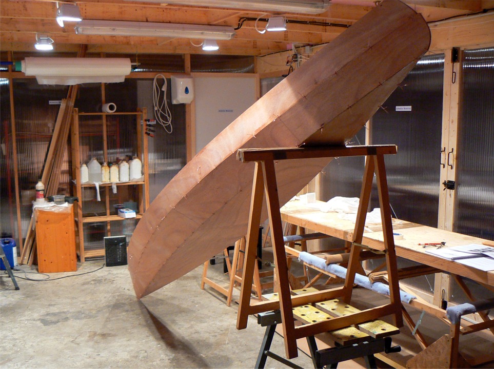 Le lendemain, l'&eacute;poxy des joints a durci et la coque est maintenant suffisamment rigide pour la jucher ainsi : la poupe est en l'air afin de couler de l'&eacute;poxy charg&eacute;e &agrave; l'int&eacute;rieur de l'&eacute;trave afin de la coller et de cr&eacute;er un petit massif au brion. En effet, c''est une zone tr&egrave;s expos&eacute;e en navigation. 