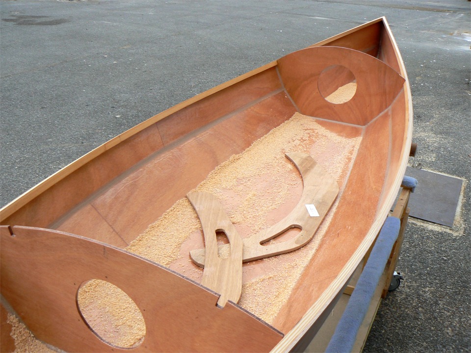 Apr&egrave;s durcissement, je remets la coque &agrave; l'endroit et je la sors dehors pour passer un coup de rabot sur les serres bauqui&egrave;res afin de leur donner un angle correspondant au bouge du pont. Celui-ci est beaucoup plus marqu&eacute; &agrave; l'avant qu'&agrave; l'arri&egrave;re, comme les observateurs avis&eacute;s l'auront not&eacute;. Les deux pi&egrave;ces en arc de cercle pos&eacute;s dans la sciure sont les "guides de rabotage" fournis avec le kit, qui permettent de v&eacute;rifier l'angle donn&eacute; aux bauqui&egrave;res. 