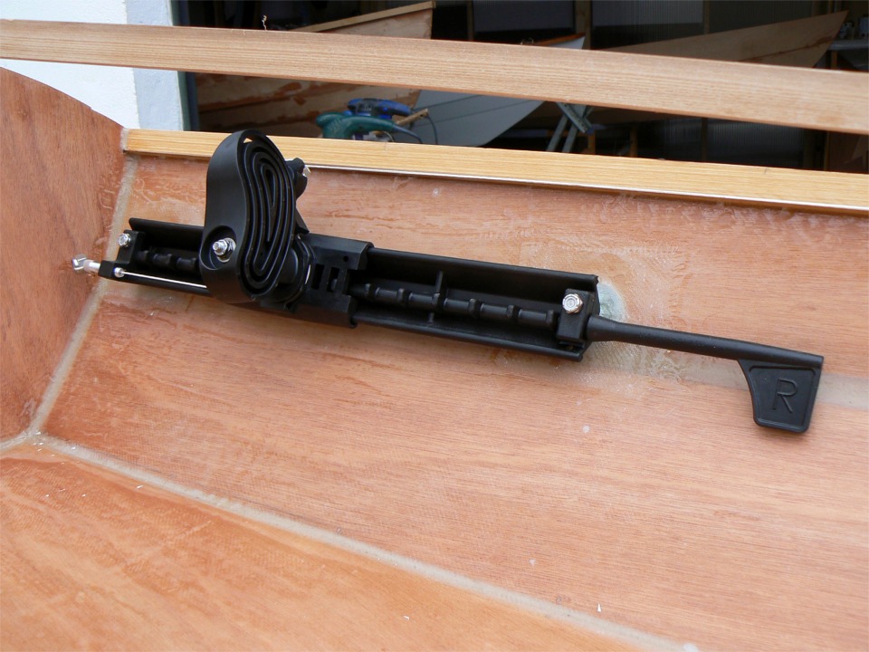 Après dépoussièrage à l'aspirateur puis à l'éponge, je remets la coque à l'endroit pour faire un essai de montage des cale-pieds. Le fil blanc tient le rôle du câble inox de commande du gouvernail afin de vérifier que la pédale coulisse librement sur le rail sans avoir à modifier le réglage de tension du câble. L'espèce de petit drapeau sur la droite permet de faire pivoter la crémaillère de blocage de la pédale pour l'avancer ou le reculer. 