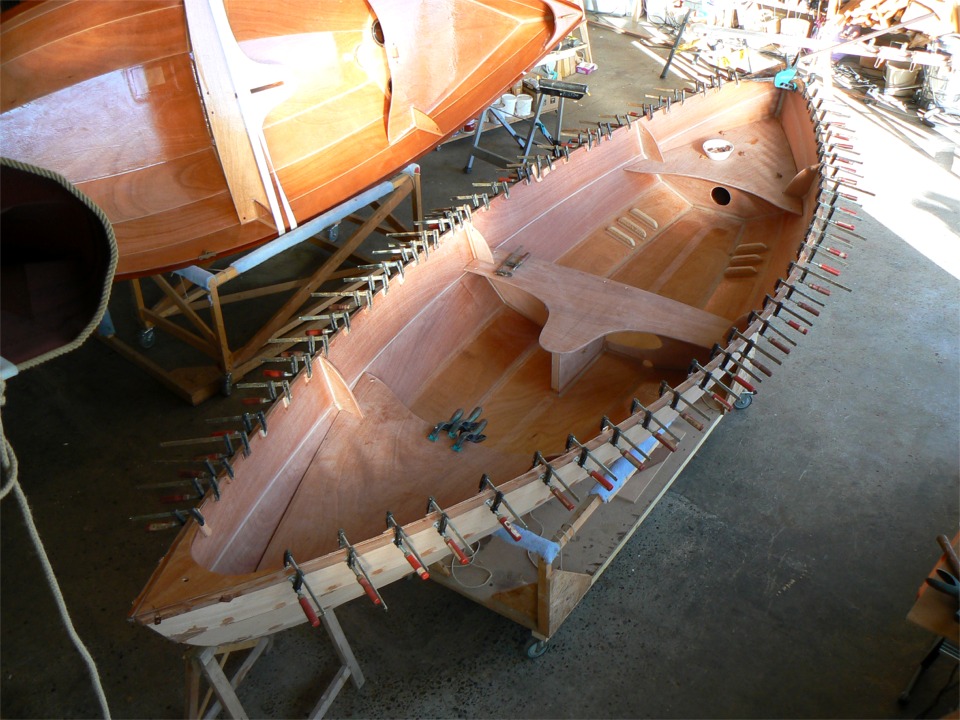 Collage du premier pli des listons sur le Skerry du Chasse-Marée . Je colle ici la première latte de chaque coté. J'ai entretemps collé en une seule opération la membrure centrale et le puits de dérive, puis fait les joints-congés dans tous les angles de cet ensemble. Le banc central et les dessus de caisson avant et arrière sont juste posés en place afin de vérifier leur ajustement. 
