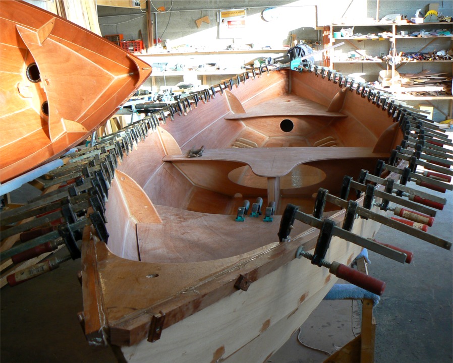 L'extrémité avant de chacun des listons est tenue par deux vis temporaires pendant le collage à l'époxy chargée, et une à l'extrémité arrière, car il n'est pas possible de poser des serre-joints à l'endroit des guirlandes. Des vis définitives en bronze fixeront le second pli en plus du collage. Il serait très difficile de cintrer les listons s'il fallait les coller en une seule fois, car leur épaisseur combinée est de l'ordre de 50 mm. Un étuvage permettrait certainement de les cinter mais ce serait bien compliqué à mettre en oeuvre pour des kits qui doivent avant tout être faciles à construire. 