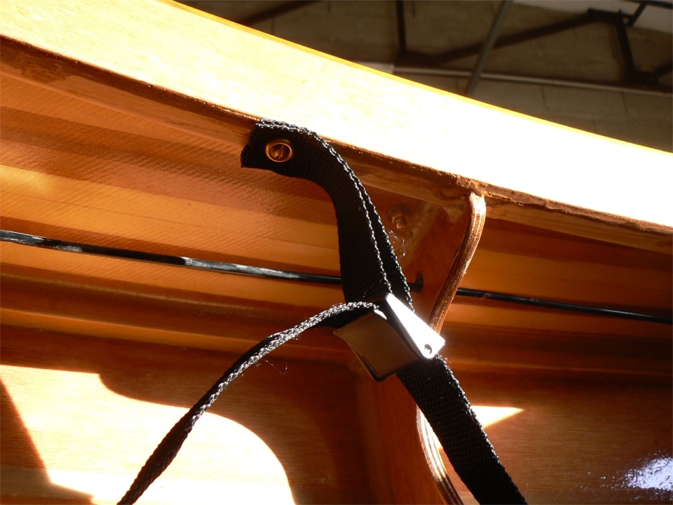 La boucle est fix&eacute; par une petite longueur de tresse plate, elle-m&ecirc;me tenue par une vis en bronze viss&eacute;e &agrave; travers une rondelle coupelle dans le dessous de l'&eacute;longis de cockpit. On voit tr&egrave;s bien la texture de la trame du tissu de verre de stratification int&eacute;rieure du pont. Le tube noir est la gaine du c&acirc;ble tribord de commande du gouvernail. L'&eacute;crou en laiton est l'un des deux qui tiennent le taquet de relevage du safran.