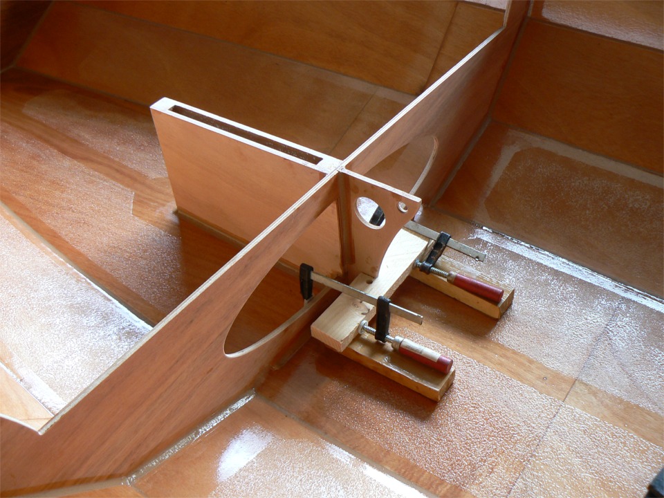 Je viens de faire tous les joints-congés autour de la membrure centrale et du puits de dérive, puis j'ai collé mon équerre grâce à cette pièce astucieuse qui me permet d'utliser deux serre-joints ancrés sur la membrure (je porte des chaussures "bateau", donc mes chevilles sont libres d'enfler selon les besoins).