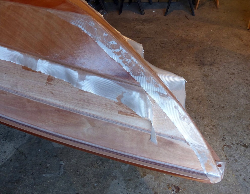 Une bande de tissu de verre d&eacute;coup&eacute;e dans les chutes est utilis&eacute;e pour recouvrir la ligne d'&eacute;trave. Je viens de poser la bande sur l'&eacute;poxy fra&icirc;che, et on voit qu'elle s'est d&eacute;j&agrave; partiellement impr&eacute;gn&eacute;e de r&eacute;sine. Nous allons maintenant finir de la saturer au rouleau jusqu'&agrave; ce qu'elle devienne totalement transparente. Notez que j'ai coup&eacute; la partie exc&eacute;dentaire de la stratification principale sur le cot&eacute; de la bande, en attendant de la couper sur le joint entre les bord&eacute;s 1 et 2.