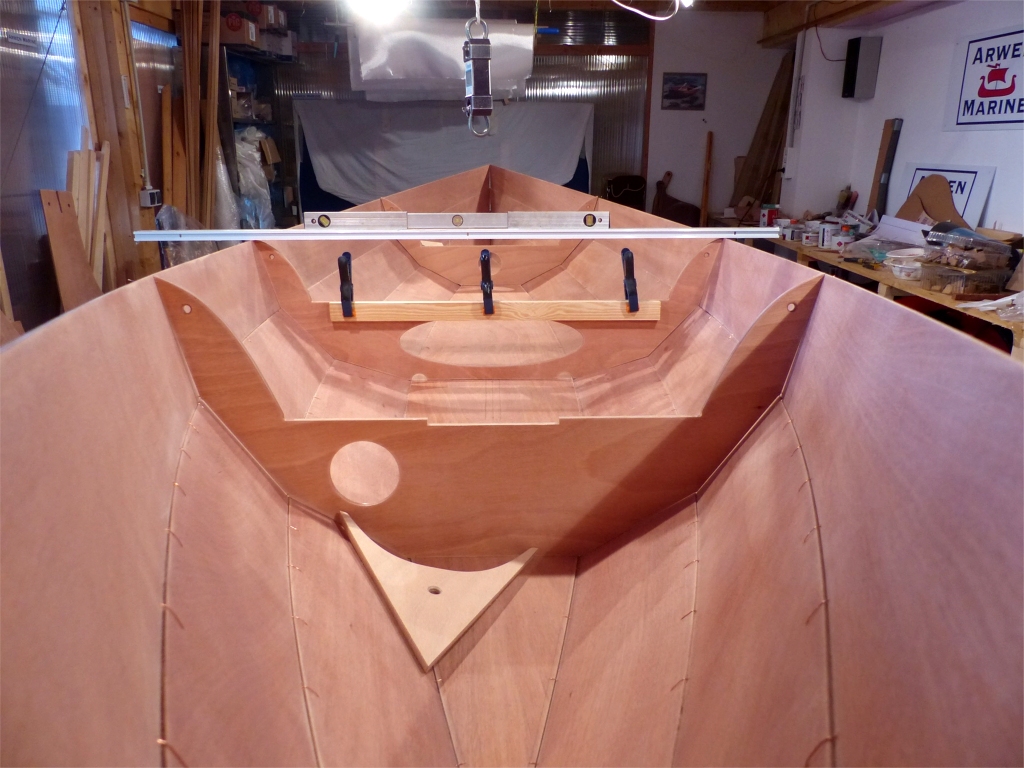 Et voici la coque totalement cousue. Notez la pr&eacute;sence de la guirlande avant, que je viens de monter avec des vis temporaires et de red&eacute;monter pour faire le gros joint-cong&eacute; de l'avant. Je la remonterai, tout comme la guirlande arri&egrave;re, d&egrave;s que les joints seront fait et avant de retourner la coque pour faire le premier collage des panneaux de coque sur l'ext&eacute;rieur. Je viens aussi de promener la r&egrave;gle et le niveau &agrave; bulle que l'on aper&ccedil;oit au milieu du bateau sur toute la longueur de la coque afin de v&eacute;rifier qu'elle n'&eacute;tait pas voil&eacute;e. Le tasseau tenu &agrave; l'aide des trois pinces aide la cloison centrale &agrave; r&eacute;sister &agrave; la pression des bord&eacute;s. 