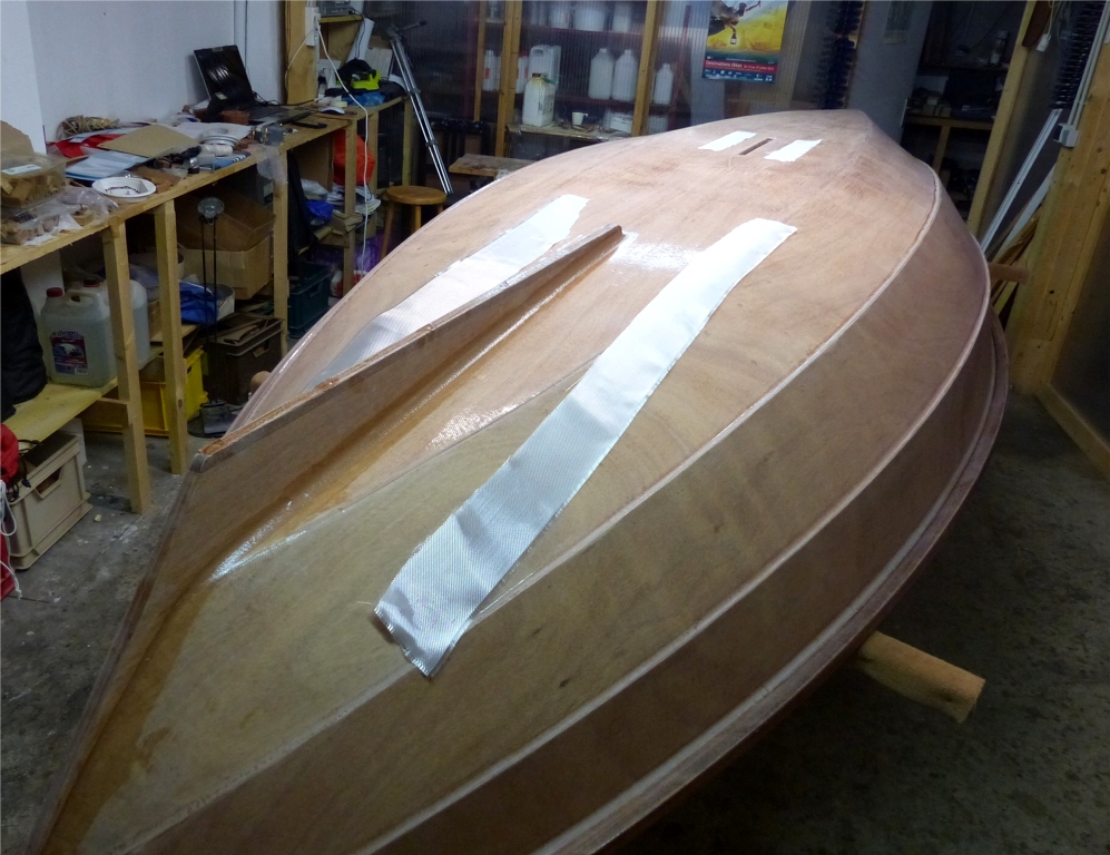 Je rentre le Skerry pour coller l'aileron, puis, apr&egrave;s avoir avoir laiss&eacute; un peu durcir l'&eacute;poxy de ses joints-cong&eacute;s, je m'appr&ecirc;te &agrave; poser dessus les bandes de renfort que l'on voit ici, en m&ecirc;me temps que de petites bandes sur le pourtour de l'ouverture du puits de d&eacute;rive, qui se trouve actuellement &agrave; nu (ouh !) Toutes ces bandes sont d&eacute;coup&eacute;es dans des chutes du tissu de verre de la stratification faite la veille. 