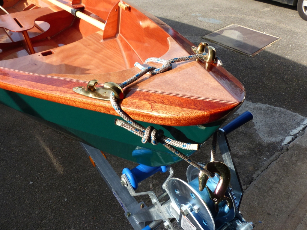 Apr&egrave;s avoir ensuite pass&eacute; les quatre couches de vernis sur toute la surface int&eacute;rieure et les listons, j'ai install&eacute; les trappes de visite des caissons &eacute;tanches et l'accastillage : les quatre supports de dames de nage, les deux chaumards asym&eacute;triques visibles ici, et les deux taquets d'amarrage en fr&ecirc;ne verni. Cette photo montre la boucle (ferm&eacute;e par un noeud de p&ecirc;cheur) qui sert &agrave; accrocher le Skerry au crochet du treuil de la remorque. La boucle passe &agrave; travers le trou de la guirlande et les chaumards la maintiennent sur les cot&eacute;s. Pour r&eacute;pondre &agrave; une question qui m'a &eacute;t&eacute; pos&eacute;e, l'essentiel de cet accastillage n'est pas inclus dans le kit complet, qui ne comporte en standard qu'une paire de supports de dames de nage (sans douille nylon) et une paire de dames de nage. Taquets et chaumards, notamment, sont absents. 