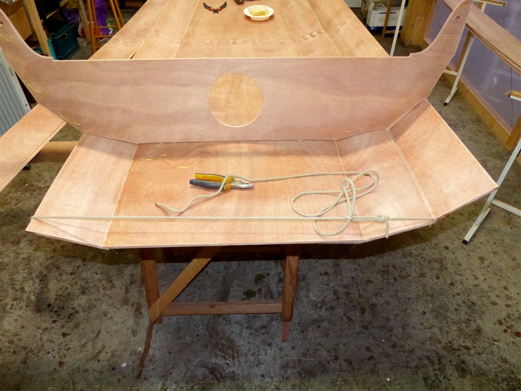 Je continue en installant les deux cloisons des compartiments &eacute;tanches, dans lesquelles j'ai d&eacute;coup&eacute; les ouvertures des trappes de 6 pouces : une pour l'arri&egrave;re et deux pour l'avant. J'ai ensuite commenc&eacute; la couture des bord&eacute;s 2 (celui de tribord est d&eacute;j&agrave; en place) et je m'aper&ccedil;ois que le cintrage de la coque fait apparaitre que les sutures entre la sole et les bord&eacute;s 1 ne sont pas assez serr&eacute;es aux extr&eacute;mit&eacute;s. J'utilise un bout de ficelle pour rapprocher les extr&eacute;mit&eacute;s et gagner le "jeu" qui me permet alors de serrer les sutures. 