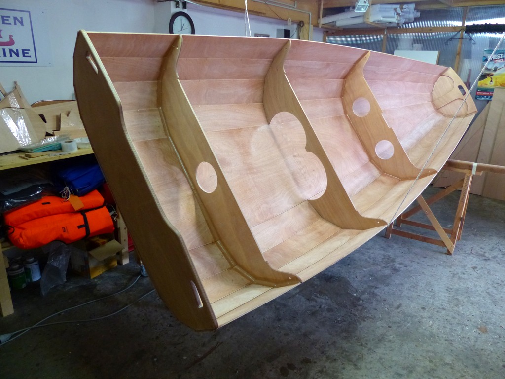 Le lendemain de ce premier collage, j'entreprends de retourner la coque seul : j'ai pass&eacute; un cordage dans deux pitons fix&eacute;s dans un chevron du plafond et l&eacute;g&egrave;rement soulev&eacute; le bateau. J'ai aussi &eacute;loign&eacute; le tr&eacute;teau arri&egrave;re et commenc&eacute; &agrave; tourner la coque. Je m'arr&ecirc;te pour faire cette photo, qui montre la coque support&eacute;e par le cordage et pos&eacute;e &agrave; l'avant. 