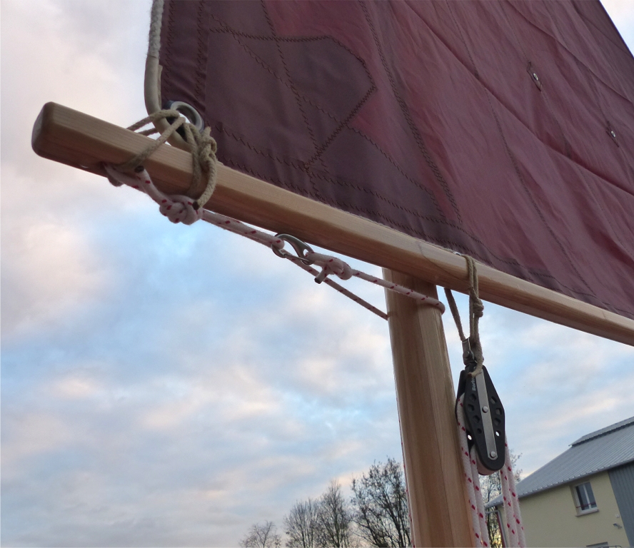 M&ecirc;me vue, cot&eacute; voile. On voit ici la poulie haute du palan d'amure &agrave; 4 brins. Son capelage est fait d'une simple boucle en cordage pass&eacute;e en double et nou&eacute;e par un noeud de p&ecirc;cheur. Un pontet inox sur le dessus de la b&ocirc;me fixe le capelage en longitudinal. Notez ma confiance absolue dans les collages &agrave; l'&eacute;poxy : le scarf est plac&eacute; &agrave; l'endroit du capelage, qui est celui de plus forte contrainte sur la b&ocirc;me ! 