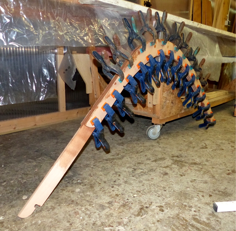 En fait, je viens de faire le second collage de l'&eacute;trave et de l'&eacute;tambot, car ces pi&egrave;ces sont constitu&eacute;es de 3 &eacute;paisseurs de contreplaqu&eacute; de 12 mm, et j'ai d'abord coll&eacute; deux &eacute;paisseurs ensemble, puis le lendemain la troisi&egrave;me sur les deux premi&egrave;res. En effet, l'exp&eacute;rience m'a appris qu'il vaut mieux &eacute;viter de presser un collage de plus de deux &eacute;paisseurs, car la couche du milieu glisse librement entre les deux ext&eacute;rieures, et on est toujours d&eacute;&ccedil;u en enlevant les pinces... La seule alternative est de cheviller &agrave; travers toutes les &eacute;paisseurs ou de les visser en plus du collage, afin de les immobiliser. J'ai pos&eacute; les pi&egrave;ces debout car leur poids combin&eacute; &agrave; celui des pinces (assez nombreuses, il est vrai) est cons&eacute;quent et je craignais de les cintrer si je les avais pos&eacute;es &agrave; plat.