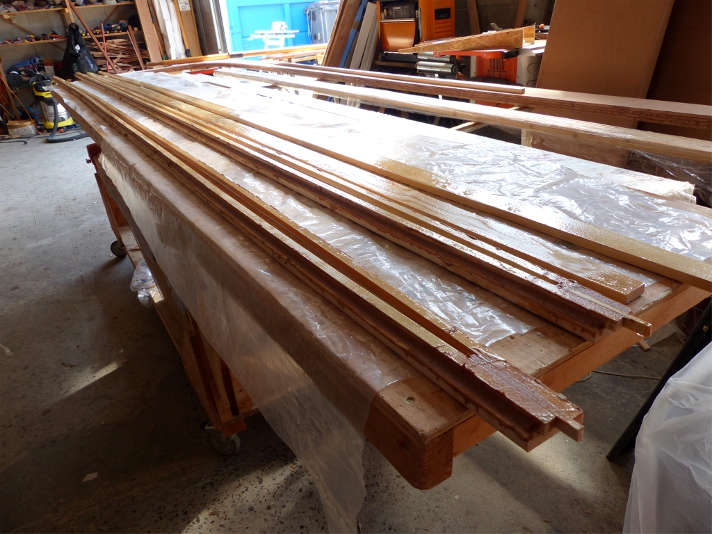 Encollage des deux faces principales du m&acirc;t. On voit aussi les deux faces secondaires, d&eacute;pourvues de lattes, mais &eacute;galement badigeonn&eacute;es d'&eacute;poxy. L'objet des lattes de 13x13 mm, outre de contribuer &agrave; la solidit&eacute; de l'ensemble, est de doubler la surface de collage sur les 4 ar&ecirc;tes du m&acirc;t, car les 4 faces ne font que 13 mm d'&eacute;paisseur, et les ar&ecirc;tes seront arrondies lors de la finition du m&acirc;t, ce qui r&eacute;duira les collages en m&ecirc;me temps que les ar&ecirc;tes. 