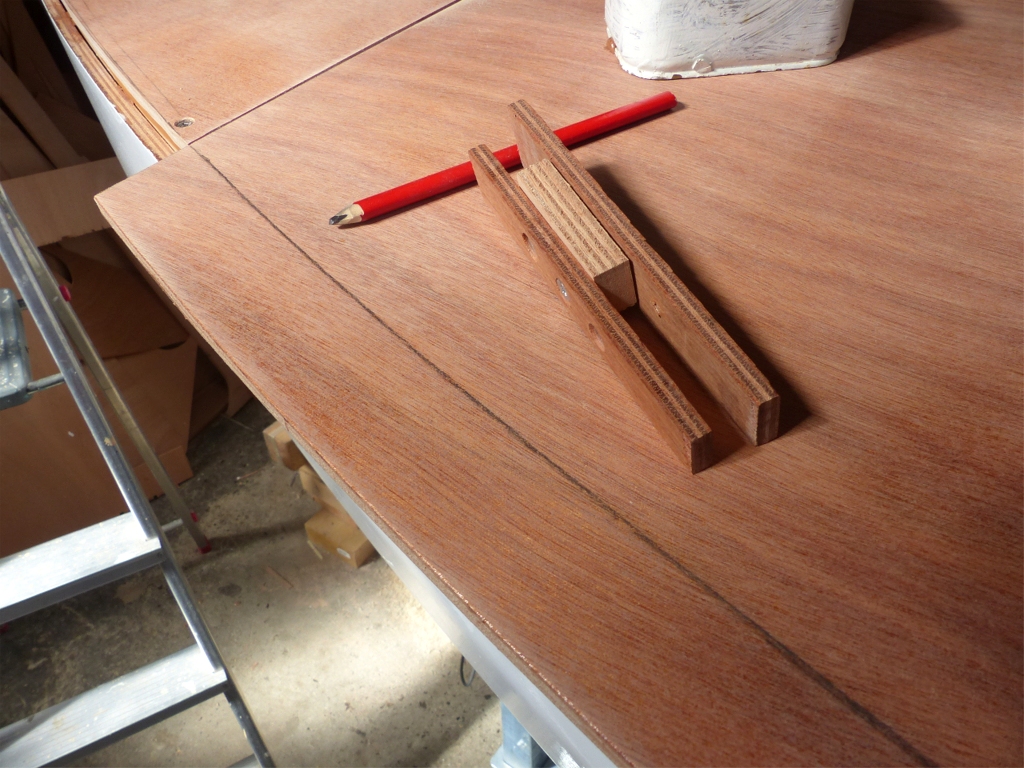 Essayage du pont lat&eacute;ral tribord. La pi&egrave;ce est tenue en place par des poids. Je viens d'utiliser le "trusquin" visible ici pour tracer la d&eacute;coupe &agrave; effectuer au droit de la face ext&eacute;rieure de la serre bauqui&egrave;re. Notez que les deux pointes de l'extr&eacute;mit&eacute; la plus proche de l'outil sont de la m&ecirc;me profondeur. Apr&egrave;s avoir fait la d&eacute;coupe, j'utiliserai son autre extr&eacute;mit&eacute;, o&ugrave; les pointes sont d&eacute;cal&eacute;es, pour tracer la ligne sur laquelle je positionnerai les vis de pourtour. 