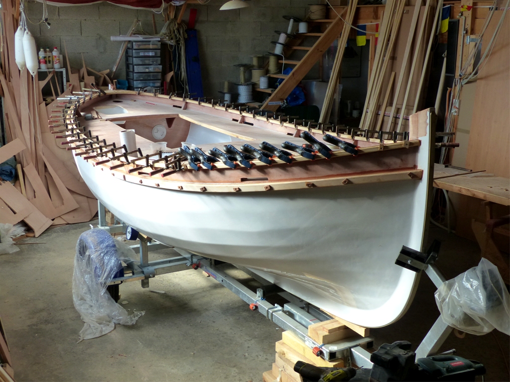 Et ce vendredi, je pose les listons bas en deux plis de 13 mm d'&eacute;paisseur. J'avais essay&eacute; la veille de poser des listons d'un seul pli de 24 mm, mais il a &eacute;t&eacute; impossible de les cintrer : j'en ai cass&eacute; un sur la forte courbure de l'arri&egrave;re et je me suis d&eacute;sist&eacute;. Le premier pli des listons visibles ici est viss&eacute; avec des vis inox, d&eacute;finitives, et le second avec des vis temporaires, reconnaissables &agrave; leur cale de contreplaqu&eacute;. Je d&eacute;monterai ces vis demain, boucherai tous les trous &agrave; l'&eacute;poxy charg&eacute;e, puis repercerai pour bouchonner. 