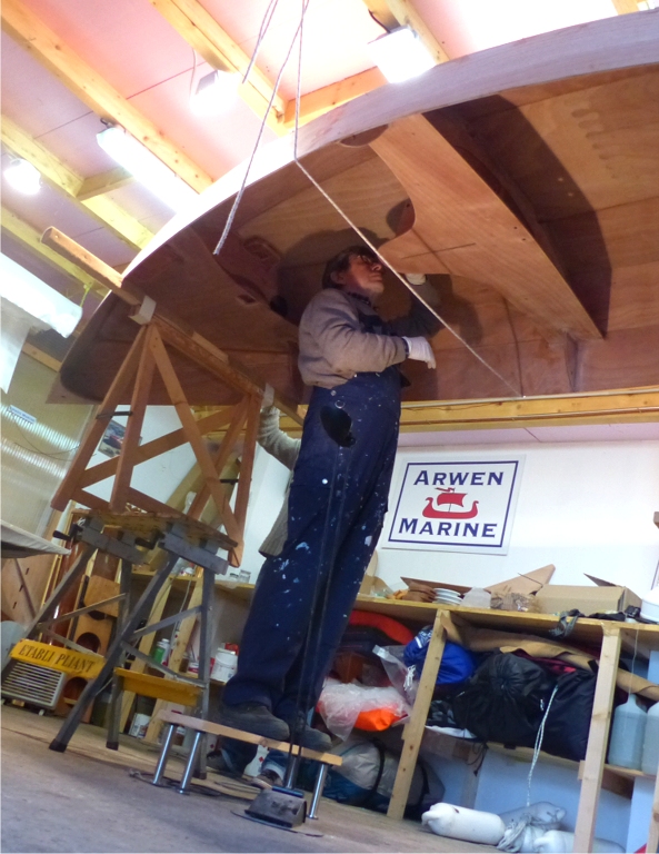 Mardi 10 : r&eacute;alisation des joints-cong&eacute;s entre le haut des cloisons et la face inf&eacute;rieure des si&egrave;ges. Le Skerry retourn&eacute; est juch&eacute; en hauteur afin d'&eacute;viter de travailler &agrave; genoux. Un cordage pass&eacute; en travers s&eacute;curise l'&eacute;chafaudage incertain. 