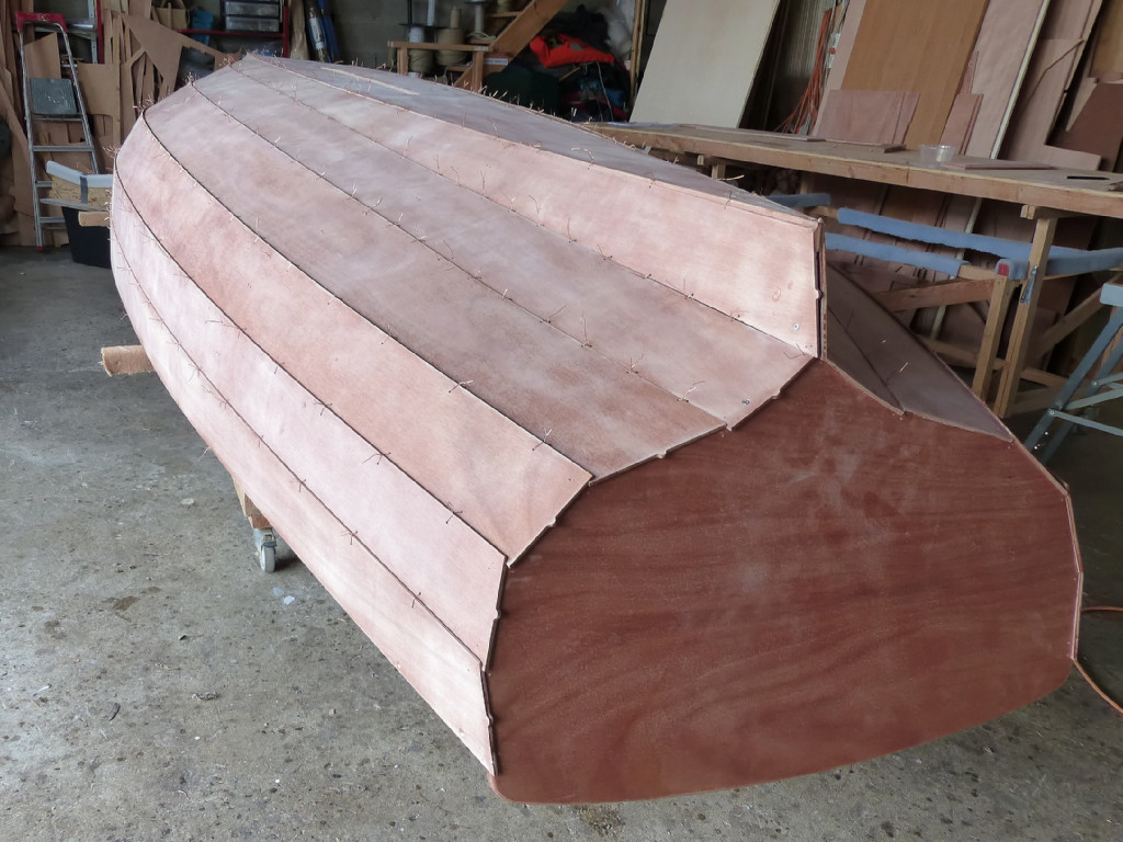 Vue générale de la coque retournée. C'est le moment de resserrer chacune des sutures. En effet, la coque retrournée se "tasse" un peu, ce qui referme les joints entre les virures, et on peut reprendre un peu de mou et s'approcher un peu plus près de la frome dessinée par l'architecte. Notez que l'extrémité arrière de tous les bordés tribord est pourvue d'un téton de repérage au centre de son bord arrière. 