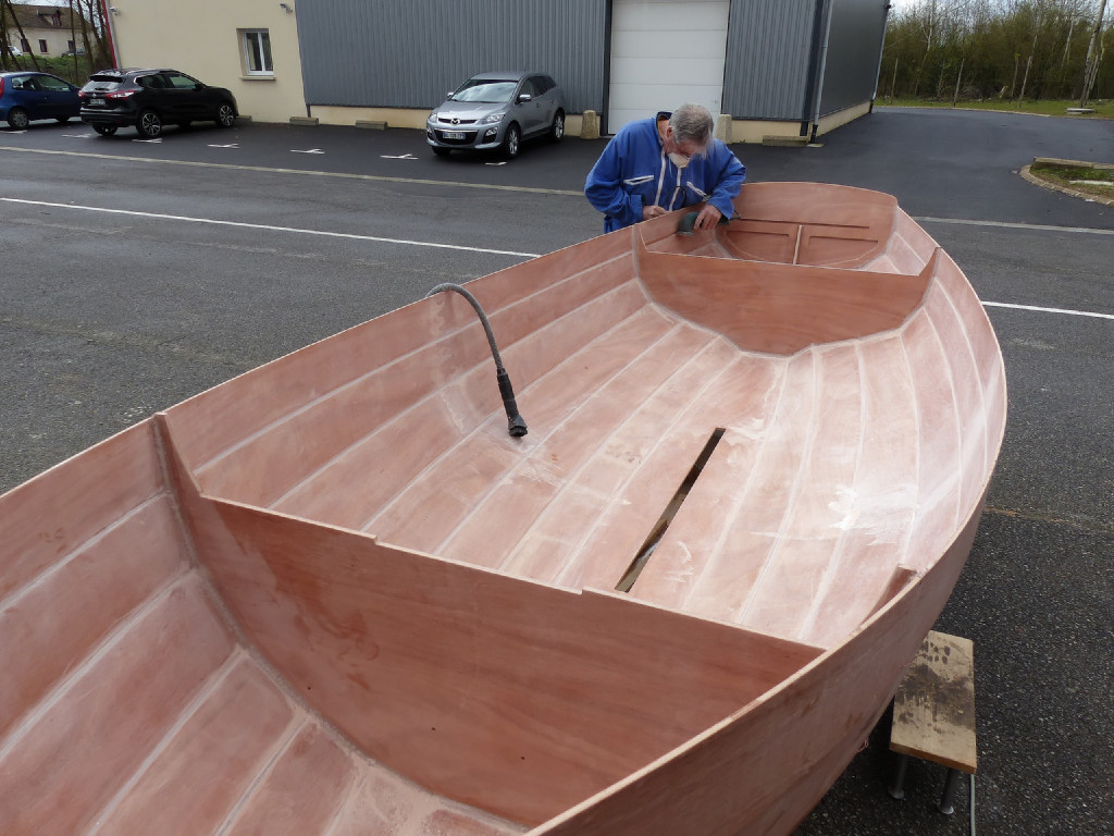 Nous sortons la coque afin de faire son premier ponçage : toute l'époxy "neuve" est poncée afin de lisser sa surface et la dépolir en vue de la suite. Si on trouve de gros pâtés que l'on a mal nettoyés durant l'opération, on peut les chauffer à l'aide du décapeur thermique et les "couper" à l'aide d'un ciseau à bois. Après le ponçage, nous passons l'aspirateur avec l'embout à brosse afin de ramasser le maximum de poussière, puis nous passons un chiffon humide sur toute la surface afin de dépoussièrer. 