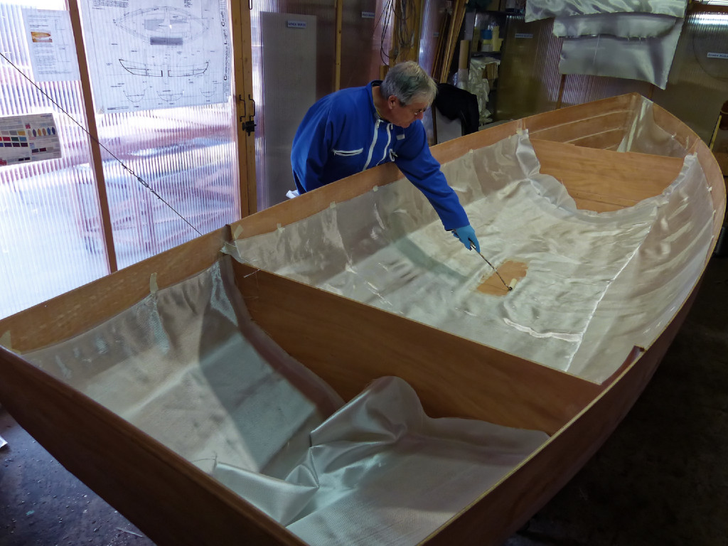 On voit que nous avons remplacé la pièce unique du coqueron arrière par deux pièces croisées comme dans el conpartiment central. A l'avant, une seule des deux pièces est en place sur tribord, celle de bâbord doit encore être posée. Benoit commence à déposer de l'époxy claire au rouleau. On doit mettre assez de résine pour que le tissu devienne totalement transparent, mais pas trop pour qu'il reste bien adhérent à la surface du contreplaqué. 