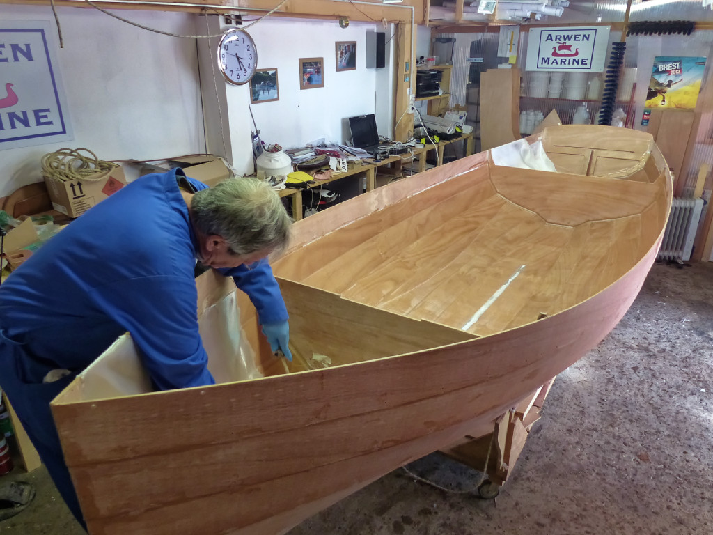 On enchaine avec les coquerons avant et arrière. Dans le coqueron avant, les deux pièces de tissu font un recouvrement au fond et dans l'étrave. De plus, une bande de biais est ajoutée en renfort depuis le haut de l'étrave jusqu'à la pointe de la sole. La bande de biais est coupée en diagonale dans une chute de tissu et sa largeur est d'une quinzaine de cm. Il est assez difficile de stratifier deux épaisseurs de tissu en même temps, et là cela fait 3 épaisseurs ! Il est tout à fait admissible de faire ce renfort lors d'une opération ultérieure, après dircissement et ponçage de la stratification. 