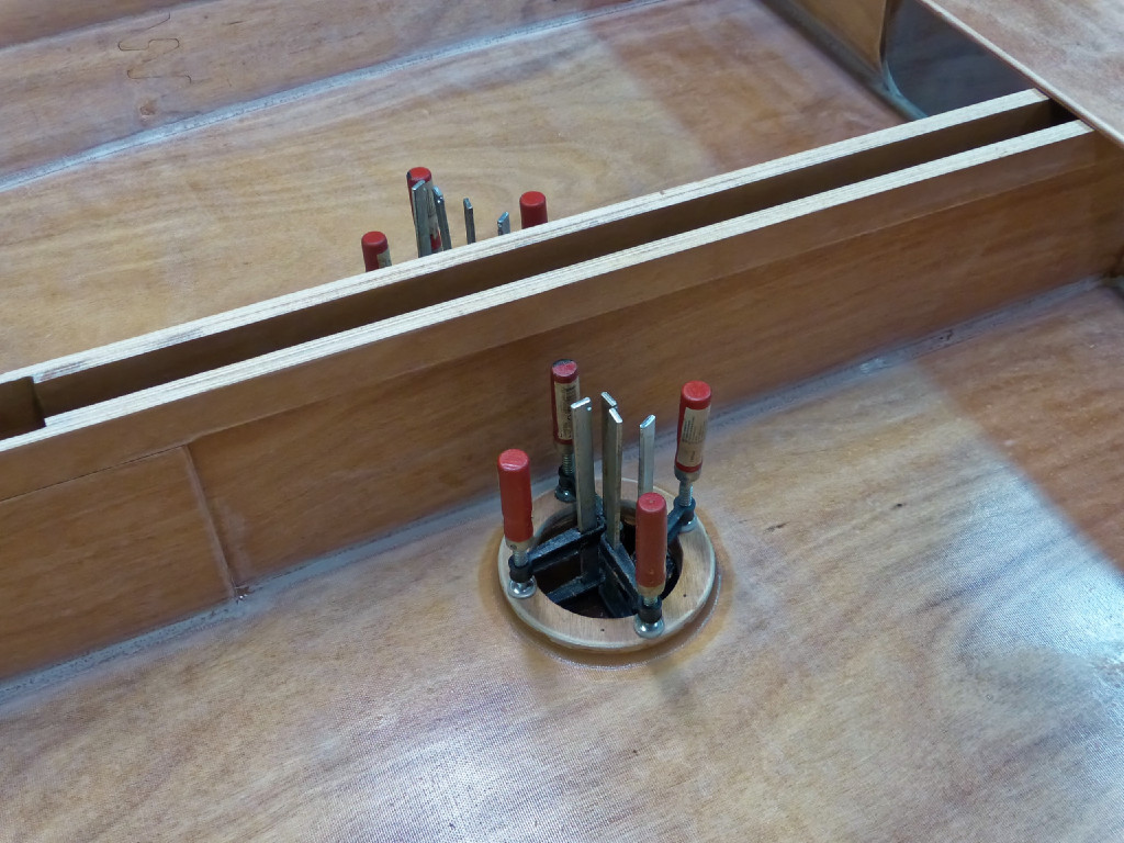 Collage des petits rehausseurs des trappes de visite de ballast. Ces pièces ne sont pas fournies dans le kit. Je les ai découpées dans des chutes (4 au total, car elles sont collées deux par deux l'une sur l'autre avant d'être collées sur le panneau). Ces rehausseurs ne sont pas indispensables, et même finalement gênants car ils se trouvent partiellement sous les matelas gonflables quand on cabane. J'ai la phobie de voir l'eau envahir le bateau si l'on ouvre ces trappes quand il est surchargé (et donc plus enfoncé su'il ne devrait), mais je pense que c'est inutile de rehausser les trappes car on ne remplirait pas le ballast si le bateau était surchargé. Je pense que je monterai les trappes directement sur le panneau pour le prochain Silmaril. Comme déjà écrit plus haut, la fonction de ces trappes est de pouvoir ouvrir ou fermer les bouchons de nable au fond des réservoirs de ballast et qui les mettent en communication avec l'extérieur et permettent de les remplir quand le bateau est à flot ou de les vider quand il est hors de l'eau. Il faut avoir à bord une pompe si on veut vider les ballasts quand le bateau est à flot. 