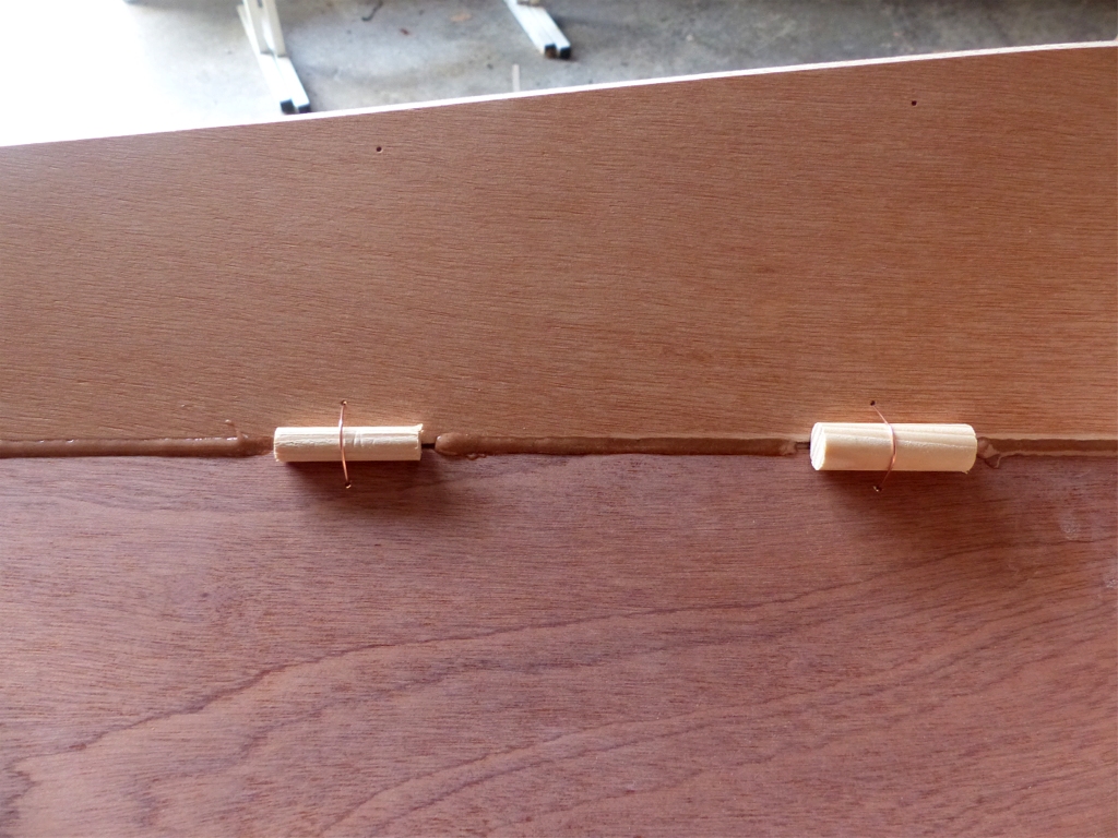 On voit ici les segments de tourillon de deux diam&egrave;tres que j'utilise (10 mm et 14 mm) pour les joints et le cordon d'&eacute;poxy charg&eacute;e que j'ai d&eacute;pos&eacute; en pointill&eacute;s le long des joints sur l'int&eacute;rieur. Ce qui est invisible, c'est que j'ai commenc&eacute; le collage sur l'ext&eacute;rieur, comme pour la coque. J'ai enchain&eacute; par l'int&eacute;rieur car la contrainte de cintrage transversal est tr&egrave;s forte &agrave; l'avant &agrave; cause du fort bouge du pont, et je crains que les panneaux se s&eacute;parent quand j'extrairai les sutures. 