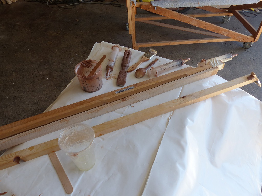 Voici les outils qui me servent &agrave; faire le joint : la pointe avant se trouvant &agrave; 1.45 m de l'avant de l'ouverture du cockpit, m&ecirc;me Mitterand n'aurait pas eu le bras assez long pour faire le joint dans la proue. J'ai donc mont&eacute; une seringue au bout d'un bout de tasseau, et j'en utilise un second pour pousser le piston et ainsi d&eacute;poser l'&eacute;poxy charg&eacute;e dans le livet, puis je lisse ce joint gr&acirc;ce &agrave; la pointe d'un troisi&egrave;me bout de tasseau (puis une cuiller quand mon bras &agrave; moi est assez long) et enfin un verre que je remplis d'&eacute;poxy "claire" pour saturer par trempage les bandes de fibre de verre qui "arment" ce joint, et un pinceau viss&eacute; au bout d'un quatri&egrave;me bout de tasseau pour d&eacute;rouler la bande satur&eacute;e sur le joint puis la lisser en place en chassant les bulles d'air. Il manque ici la lampe frontale qui me permet de voir ce que je fais. 