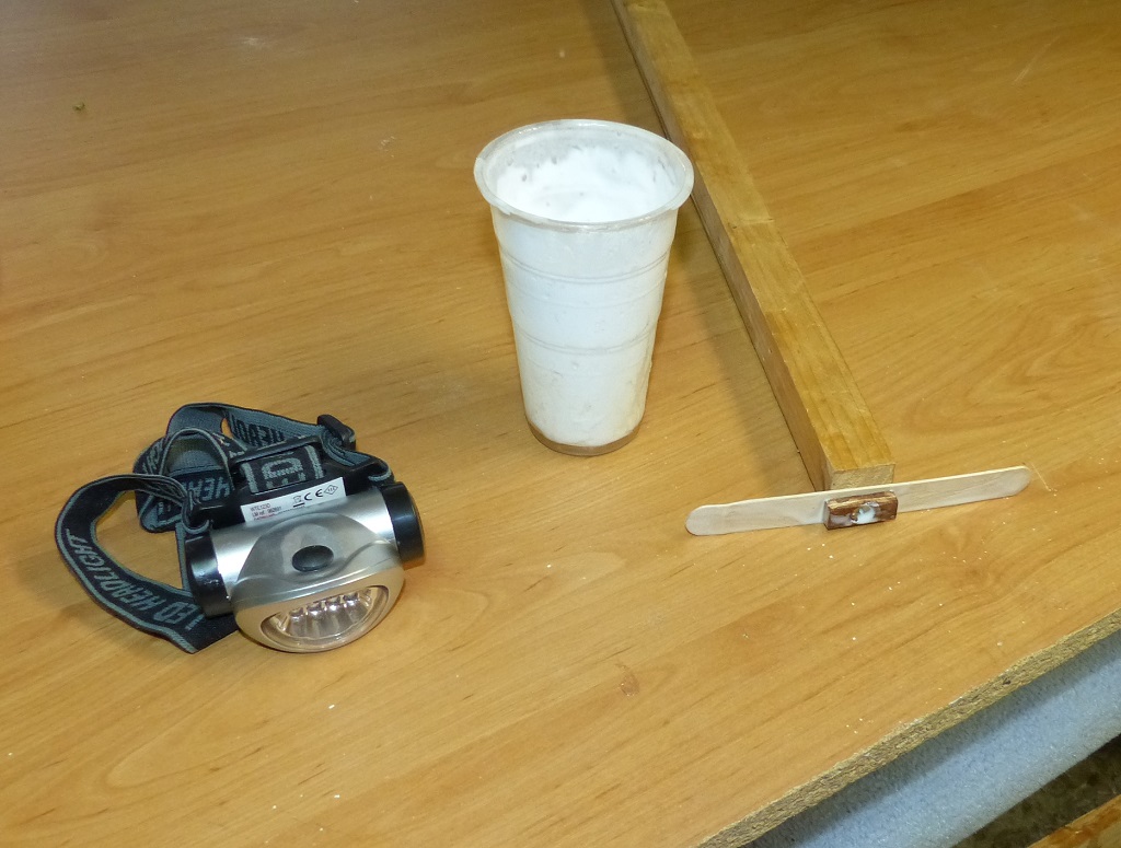 Voici mes outils pour cette op&eacute;ration : un verre de 180 ml d'&eacute;poxy &agrave; laquelle j'ai ajout&eacute; une charge basse densit&eacute; (micro sph&egrave;res de verre) pour ne pas trop alourdir les extr&eacute;mit&eacute;s du kayak, une lampe frontale pour voir ce que je fais et enfin une raclette bricol&eacute;e avec un "b&acirc;ton d'eskimo", un bout de tasseau et une vis passant &agrave; travers une cale de CP. 