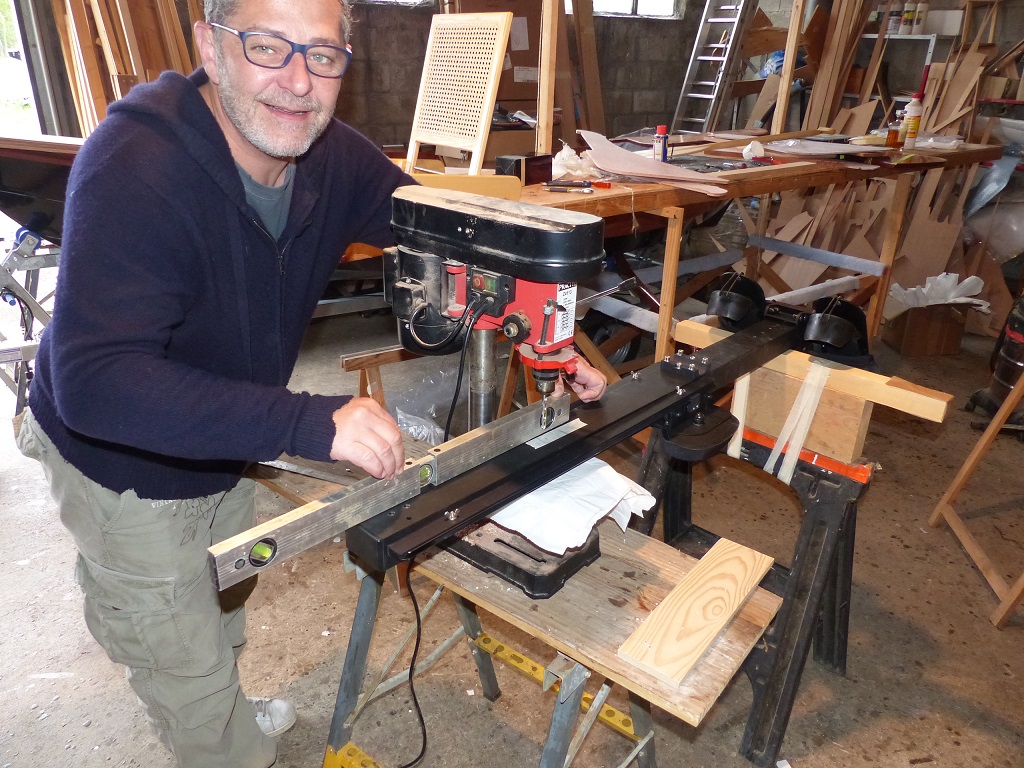 On commence par percer l'extr&eacute;mit&eacute; arri&egrave;re su rail, puis on marque pour le second trou, et on perce ! La difficult&eacute; pour ces deux per&ccedil;ages et d'&ecirc;tre parfaitement vertical, car on doit en fait superposer deux trous &agrave; travers le rail du banc de nage et le trou &agrave; travers la cale fix&eacute;e sur la membrure. Nous utilisons donc la perceuse &agrave; colonne avec un syst&egrave;me de calage ad hoc. Olivier v&eacute;rifi&eacute; ici l'horizontalit&eacute; du dispositif avant de percer. 