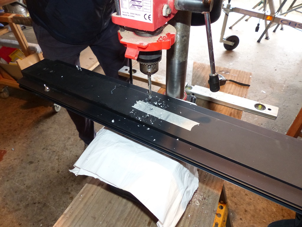 Le bout de bande de masquage coll&eacute; sous le rail nous a permis de marquer visiblement &agrave; travers le trou de la membrure sous le rail. L'essuie-tout sous le rail permet d'&eacute;viter de marquer l'anodisation noire impeccable du rail en le bougeant sur la platine de la perceuse. 