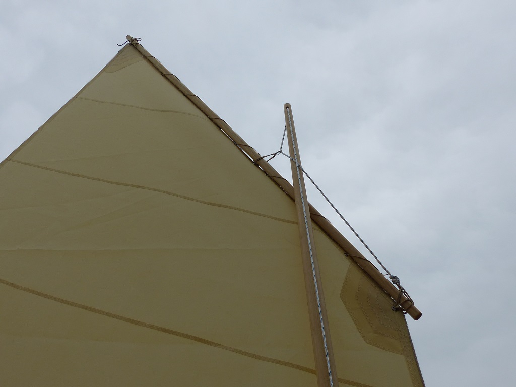 Cette vue de la vergue et de la t&ecirc;te de m&acirc;t montre le montage "australien" de la drisse. La drisse est frapp&eacute;e par un mousqueton sur un erseau fix&eacute; sur le talon de la vergue. Elle passe ensuite par un second mousqueton fix&eacute; par un second erseau capel&eacute; un peu en arri&egrave;re du tiers avant de la vergue. Notez que la drisse passe du c&ocirc;t&eacute; oppos&eacute; du m&acirc;t, plaquant ainsi la vergue contre celui-ci, tout en lui laissant une grande libert&eacute; de mouvement longitudinal lorsque la drisse est mollie. 