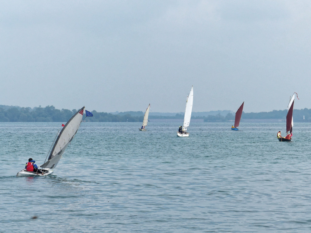 La plage se couvre peu &agrave; peu de bateaux pr&ecirc;ts &agrave; prendre la mer (j'ai essay&eacute;, mais "prendre le lac" parait bizarre...) De gauche &agrave; droite, le Doryplume "Prise de Ris'k" de Bernard, le Skerry Raid "Truk" d'Yves, mon Goat Island Skiff (en raccourci GIS) "Let's Goat!", et le Skerry "L'Odet"Et c'est parti ! Au premier plan &agrave; gauche, c'est Marco &agrave; bord de son cano&euml; &agrave; voile "Tasu". Il l'a construit lui-m&ecirc;me en pliant et rivetant des t&ocirc;les d'aluminium car son allergie &agrave; l'&eacute;poxy lui interdit dor&eacute;navant la construction en CP-&eacute;poxy. 