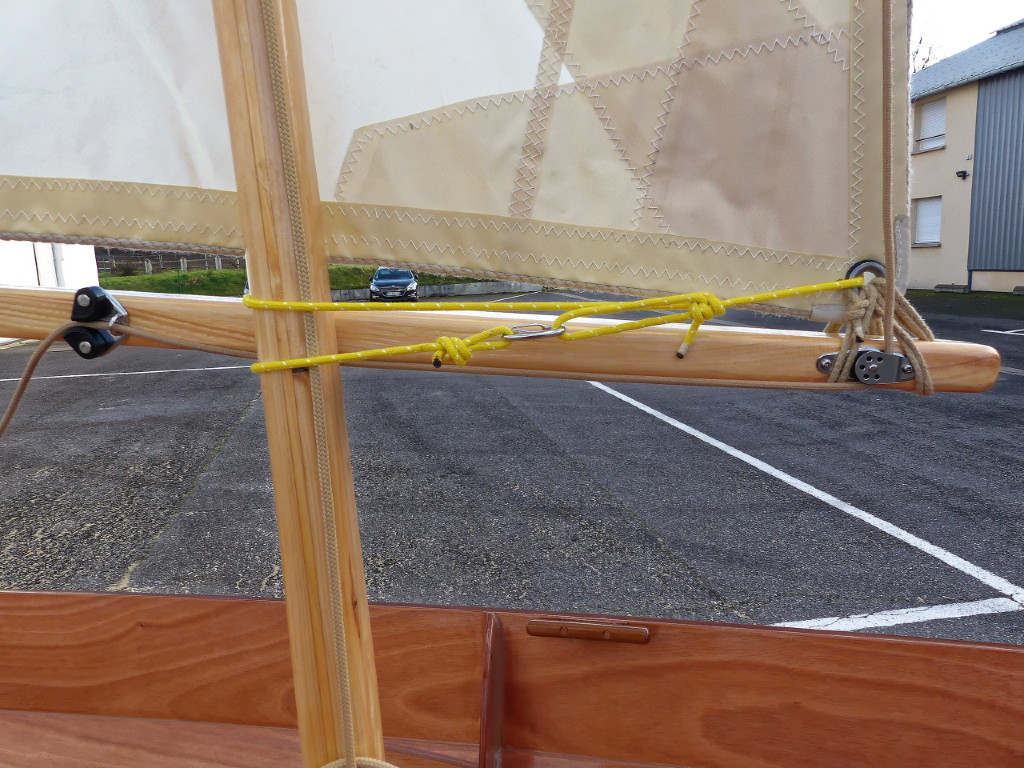 Bêleur en place : l'extrémité longue passe autour de la bôme derrière le mât et on frappe le mousqueton sur la boucle réglable de l'autre extrémité.