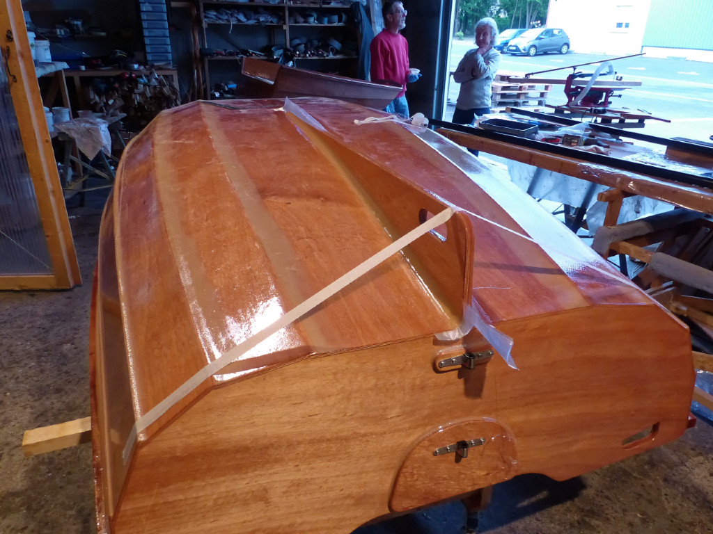 Dernière opération de la construction du PassageMaker Dinghy : le collage de son grand aileron. Nous avons renforcé les joints-congés qui le tiennent par des bandes de fibre de verre. 
