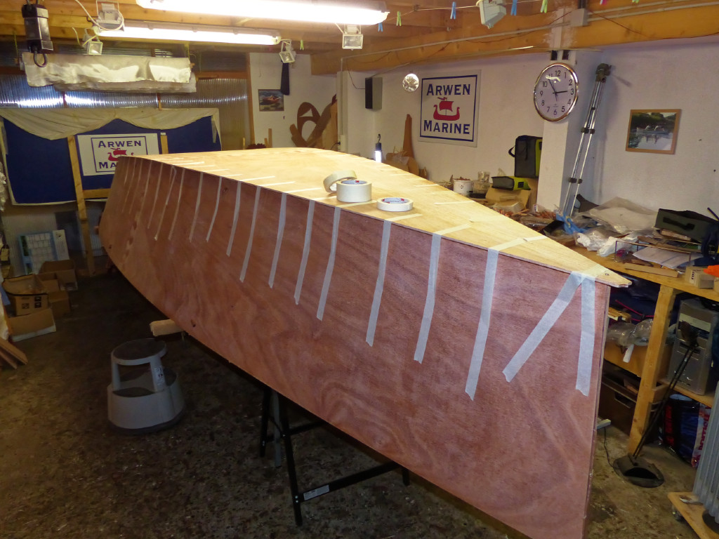 Le lendemain, après durcissement des joints-congés, nous retournons ce début de coque et le réalignons soigneusement avant de poser le panneau de fond dessus, puis de le coller à la bande adhésive le long de ses bords. Quelques vis temporaires assurent qu'il ne bougera pas latéralement. 