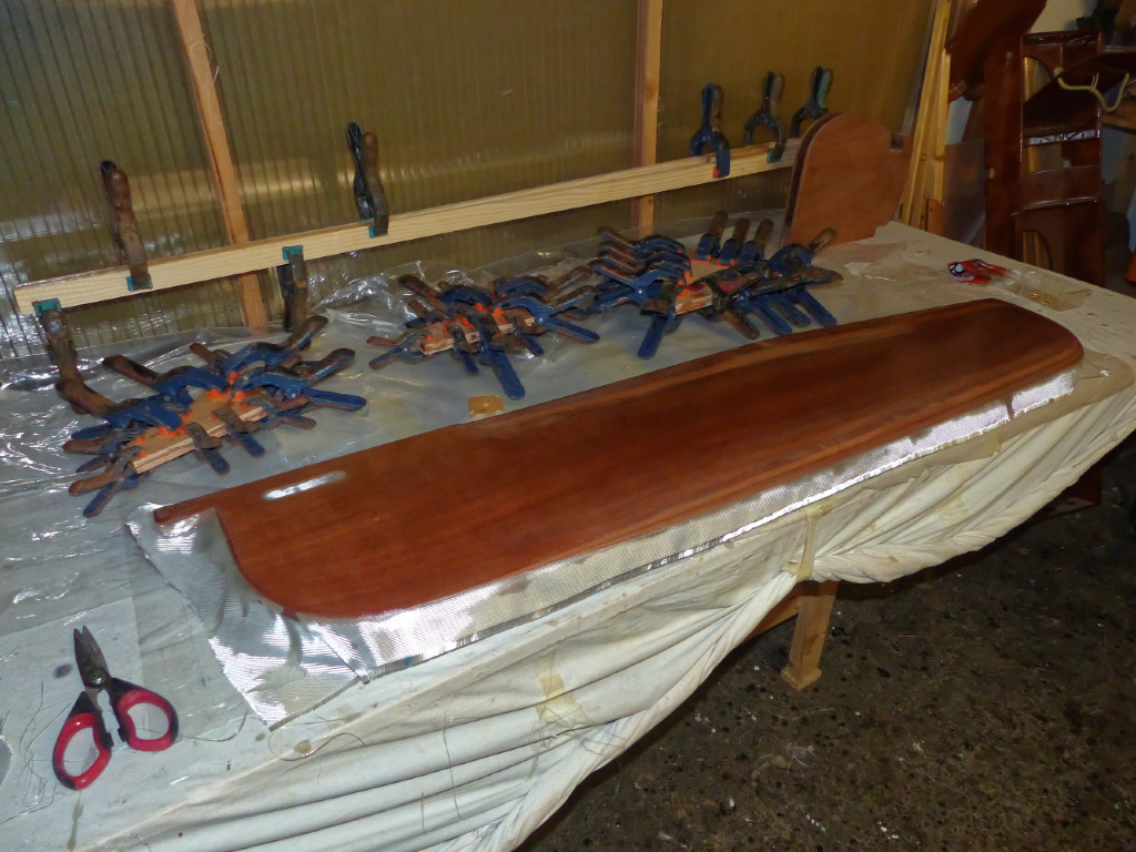 Stratification de l'une des faces de la sérive et collage des deux plis de la guirlande et des courbes arrière, ainsi que de la longue barre La découpe dans le haut de la dérive forme une poignée qui permettra de l'extraire plus facilement. Pierre a constaté que c'est une opération que l'on fait souvent à la volée, juste avant d'aborder sur une plage. En effet, il est imprudent de laisser la dérive repliée dans son puits quand il y a du ressac car elle se bloque en quelques instants à cause des petits cailloux qui vienne se coincer entre la dérive et les parois du puits. 