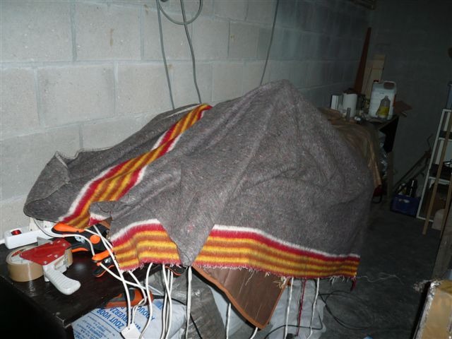 Pour le durcissement optimal de l'&eacute;poxy, Patrick emmaillote ses collages dans une couverture chauffante &eacute;lectrique, et ajoute par-dessus une couverture "normale". Les poign&eacute;es des pinces et presses ou deux-trois bouts de tasseau servent &agrave; cr&eacute;er une poche d'air et &eacute;viter de coller la couverture chauffante avec les pi&egrave;ces. Simple et &eacute;l&eacute;gant... hum, peut-&ecirc;tre pas tr&egrave;s &eacute;l&eacute;gant mais diablement efficace : 22&deg;C &agrave; l'int&eacute;rieur ! 