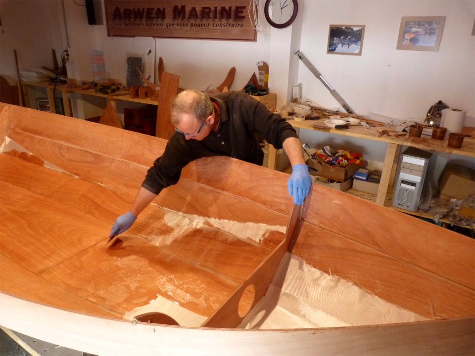 Herv&eacute; utilise la "squeegee" pour &eacute;taler la r&eacute;sine et la faire p&eacute;n&eacute;trer dans le tissu de verre, qui devient ainsi transparent. On voit que la stratification ne couvre que la sole et la premi&egrave;re paire de bord&eacute;s. En effet, c'est le fond du bateau qui est &agrave; la fois le plus maltrait&eacute; (&agrave; l'ext&eacute;rieur par les contacts avec des surfaces dures et &agrave; l'int&eacute;rieur sous les semelles de l'&eacute;quipage) et le plus solicit&eacute; afin de rigidifier la coque. Cette stratification int&eacute;rieure sera compl&eacute;t&eacute;e par une stratification sur l'ext&eacute;rieur de la coque, &eacute;galement limit&eacute;e &agrave; la sole et les deux bord&eacute;s bas. 
