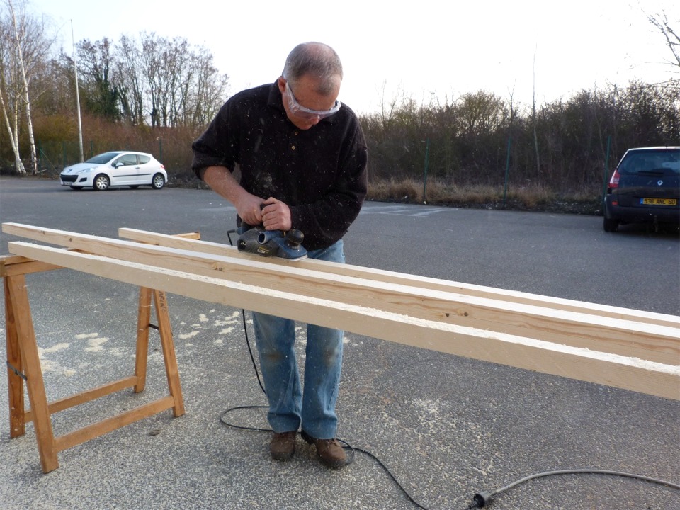 Herv&eacute; rabote les espars de son gr&eacute;ement &agrave; misaine au tiers : b&ocirc;me, m&acirc;t et vergue. Ceux-ci sont constitu&eacute;s de deux &eacute;paisseurs de sapin contrecoll&eacute;es. Nous avons tout d'abord affin&eacute; les extr&eacute;mit&eacute;s de ces espars sur la scie de table, et Herv&eacute; est occup&eacute; &agrave; "lisser" ces 4 faces au rabot, avant de tailler 4 nouvelles faces en rabattant les ar&ecirc;tes. 