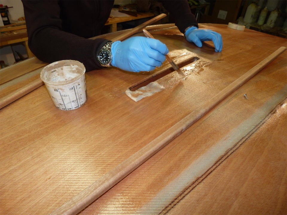 Jean sature au pinceau les petites bandes de fibre de verre que nous posons sur le pourtour de l'ouverture du puits de d&eacute;rive. Nous avions stratifi&eacute; la face interne des deux joues du puits avant de le monter. Ce n'est pas pr&eacute;vu dans le manuel de construction, mais je troue que c'est une bonne id&eacute;e car on n'ira plus gu&egrave;re inspecter ou r&eacute;parer l'int&eacute;rieur du puits de d&eacute;rive. 