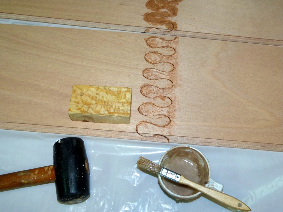 J'ai ensuite utilisé le maillet pour suggérer aux deux parties du puzzle de s'emboiter l'une dans l'autre. J'ai tapé sur la cale en pin que l'on aperçoit près du maillet afin de ne pas abîmer la surface du contreplaqué. J'ai posé la cale à l'envers afin d'éviter de tacher hors de la zone de collage. En effet, il s'agit de la face intérieure des bordés, que je compte vernir. 