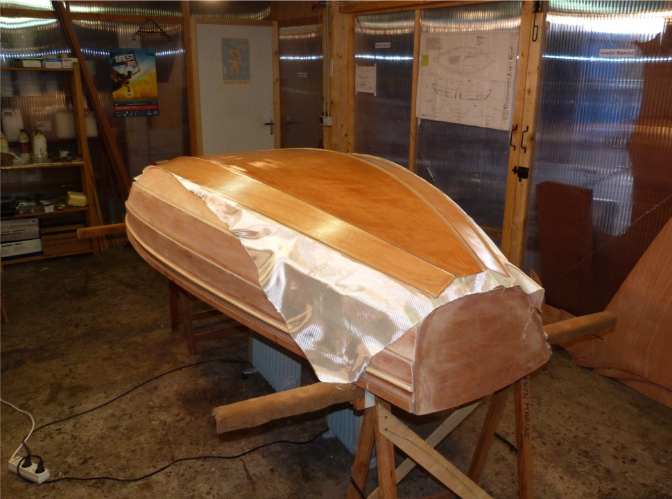 Apr&egrave;s un pon&ccedil;age soign&eacute; (et rafraichissant, car je ponce toujours &agrave; l'ext&eacute;rieur afin d'&eacute;viter de re-respirer toute la poussi&egrave;re. Il y a des jours o&ugrave; je me demande si &ccedil;a ferait vraiment mal &agrave; mes poumons), je passe &agrave; la stratification de l'ext&eacute;rieur de la coque : comme &agrave; l'int&eacute;rieur, ce ne sont que la sole et les deux bord&eacute;s 1 qui sont recouverts de tissu de verre. J'ai satur&eacute; d'&eacute;poxy le tissu sur toute la surface stratifi&eacute;e (ce qui l'a rendu transparent), et vais maintenant couper l'exc&eacute;dent de tissu sur les bords. 