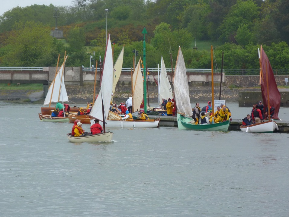 En me rendant sur le port de Vannes ce matin, je tombe sur la flottille n°2 (Voile-aviron) en train de sortir du canal d'accès du port de Vannes pour le début de la première journée de navigation. Le pont que l'on aperçoit à l'arrière-plan (et qui peut s'ouvrir en pivotant une partie du tablier) est juste un peu bas pour le mât de "Piff", le Skerry de Jean-David. 