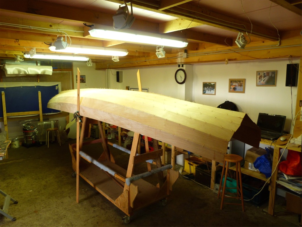 Apr&egrave;s pon&ccedil;age, je perce les quelque 420 trous pour les sutures, sachant que pour chacun de ces trous je percerai un jumeau au moment de la couture, puis je commence &agrave; coudre la coque renvers&eacute;e sur un portique mont&eacute; sur le chariot. Les b&eacute;quilles lat&eacute;rales supportent les cot&eacute;s de la coque et l'aident &agrave; prendre son volume, sachant que l'&eacute;trave (cach&eacute;e &agrave; l'arri&egrave;re-plan) est aussi ouverte &agrave; ce stade que l'arri&egrave;re. 