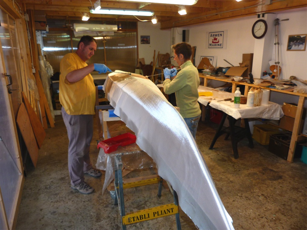 Annick et Emmanuel commencent à saturer le tissu de verre au rouleau en partant du milieu et en progressant vers les extrémités de façon plus ou moins symétrique. 