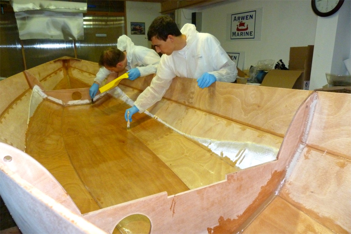 Nous avons remis la coque à l'endroit et fait tous les joints intérieurs et bouché les trous des sutures sur la surface intérieure. Nous enchainons avec la stratification : un tissu de verre est lié à la surface du contreplaqué en le saturant de résine époxy à l'aide de rouleaux. 