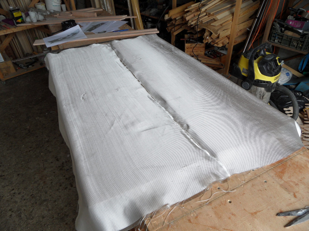 Nous allons stratifier un certain nombre de pièces afin de protéger et rigidifier leur surface. Ici, ce sont les deux "joues" du puits de dérive qui sont stratifiées sur leur surface intérieure, qui sera soumise aux frictions de la dérive et du sable ou des petits cailloux qui entreront dans le puits et sera difficile à inspecter et entretenir. on découpe le tissu de verre et on le drape sur la surface... 