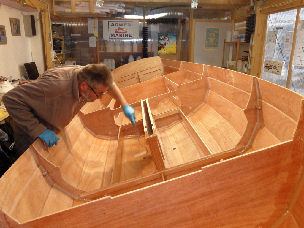 Nous allons maintenant passer au collage des planchers. Le bateau est encore si léger que je l'incline simplement en appuyant sur le haut du bordage. Je commence par passer une nouvelle couche d'époxy sur la surface intérieure des réservoirs de ballast et des caissons étanches. On ne laissera pas durcir cette couche d'époxy, on va coller les planchers dans la foulée, après avoir aussi fait une couche d'époxy "fraîche" sur leur surface intérieure. 