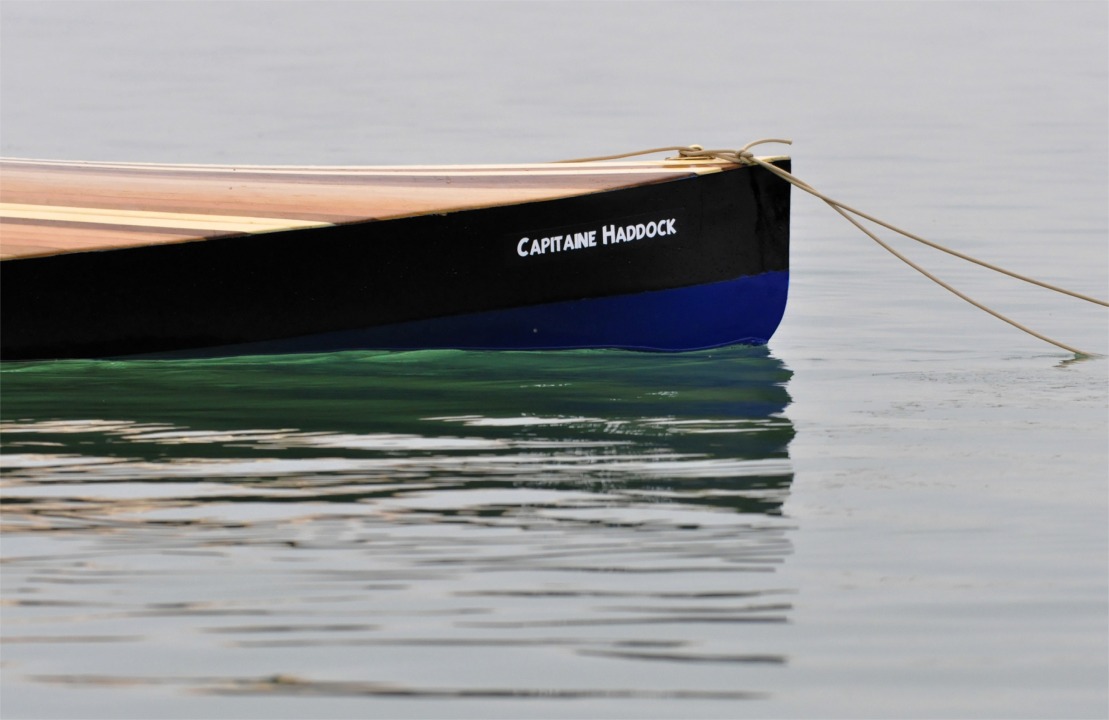 La proue du magnifique Wood Duck 12 hybride "Capitaine Haddock" construit par Christophe cet hiver. Notez les couleurs de coque : bleu comme le pull et noir comme le costume d'Archibald, ainsi que la police de caractères du nom, identique à celle des titres des albums d'Hergé.